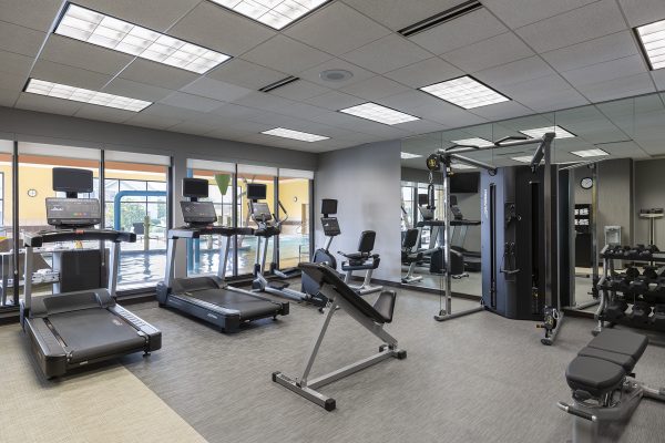 A gym room with tread machines and mirrors.