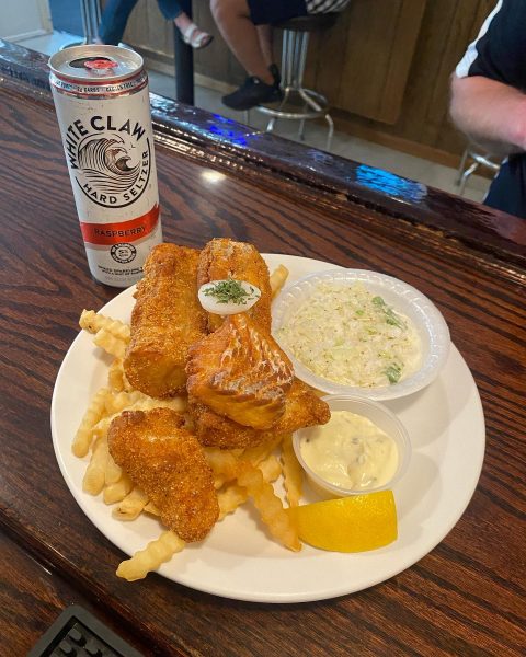 A plate of fish and chips and a beer on a bar.