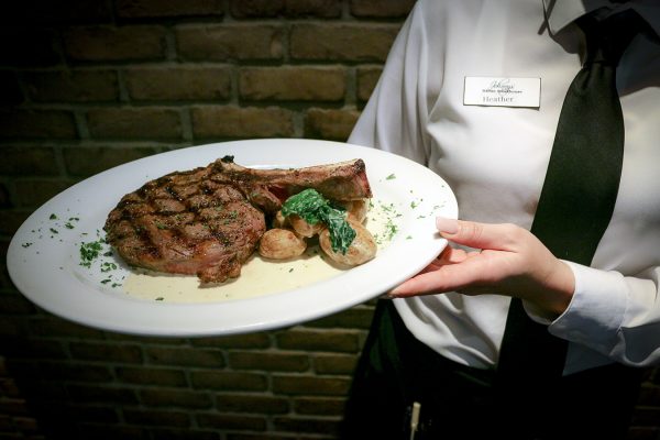 A waiter holding a plate with a steak and vegetables.