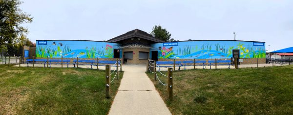 A building in Middleton with blue murals depicting aquatic life, surrounded by grass, a rope fence, and hints of nearby waterslides, all under a cloudy sky.