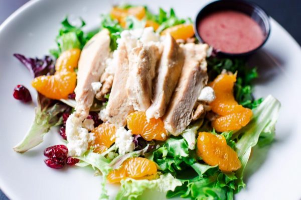 a plate of chicken salad with oranges and cranberries.