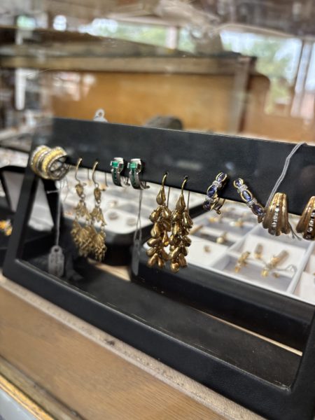 A display of assorted earrings, including gold dangles and gemstone studs, arranged on a black stand in the University Coin & Jewelry store showcase.