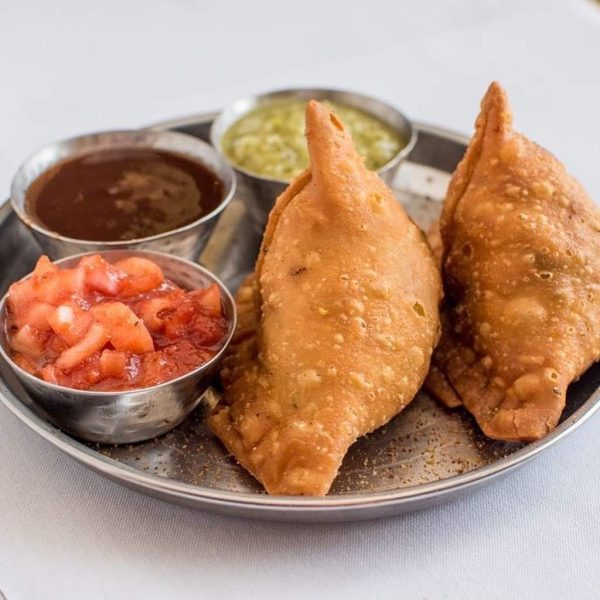 A plate of samosas with dipping sauces on it.