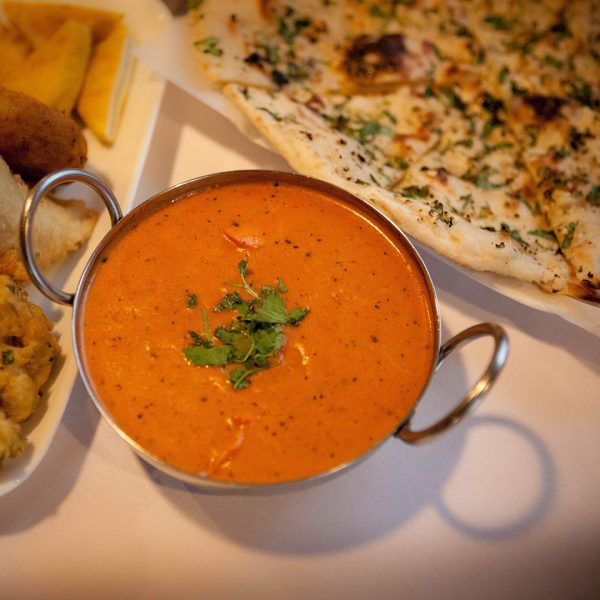 A plate of indian food on a table next to a bowl of soup.