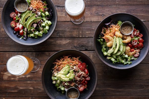 Three bowls of food and beer on a wooden table.