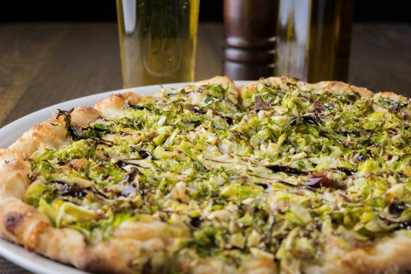 A pizza with brussels sprouts on a plate next to a glass of beer.