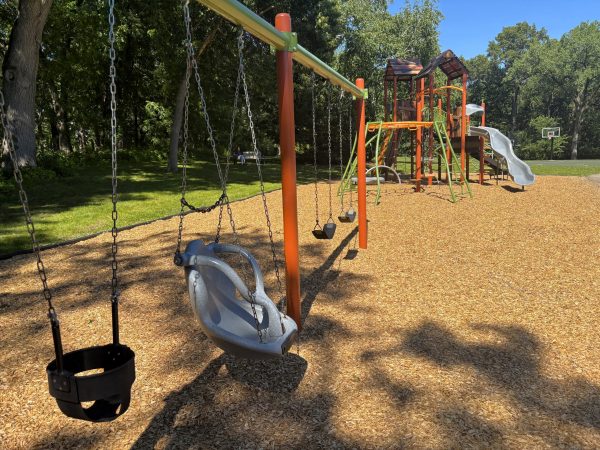 Middleton Park features a playground with multiple swings, a climbing structure, and slides, all set on wood chips and surrounded by trees on a sunny day.