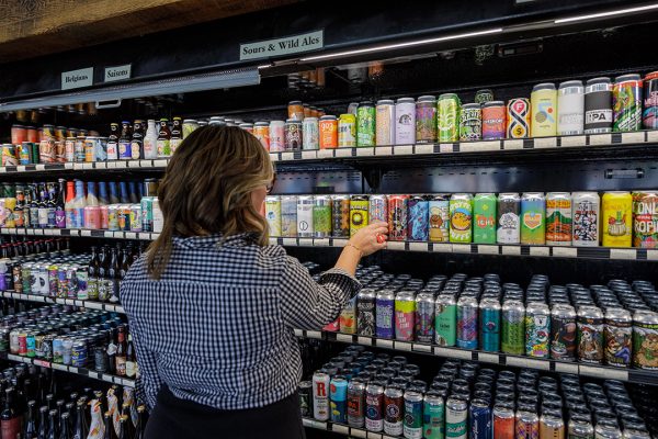 A woman is standing in a store looking at cans of beer.