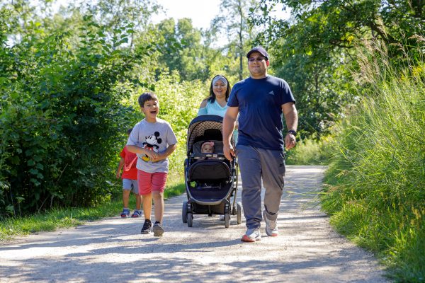 A family, man, woman, young boy and child in stroller, walking down path in Pheasant Branch Conservancy in Middleton.