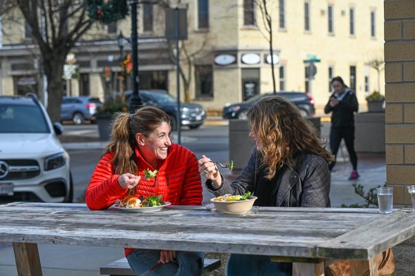 Two women sitting at a table eating a bowl of salad.