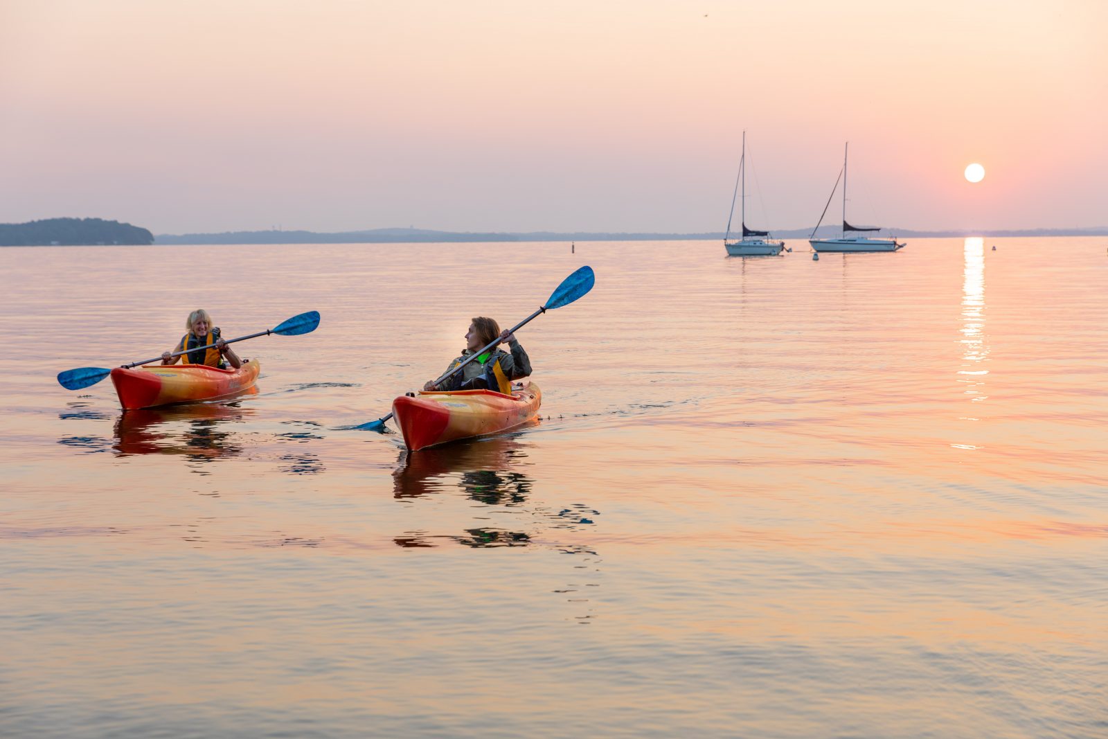 Two people paddling kayaks in the water at sunset.
