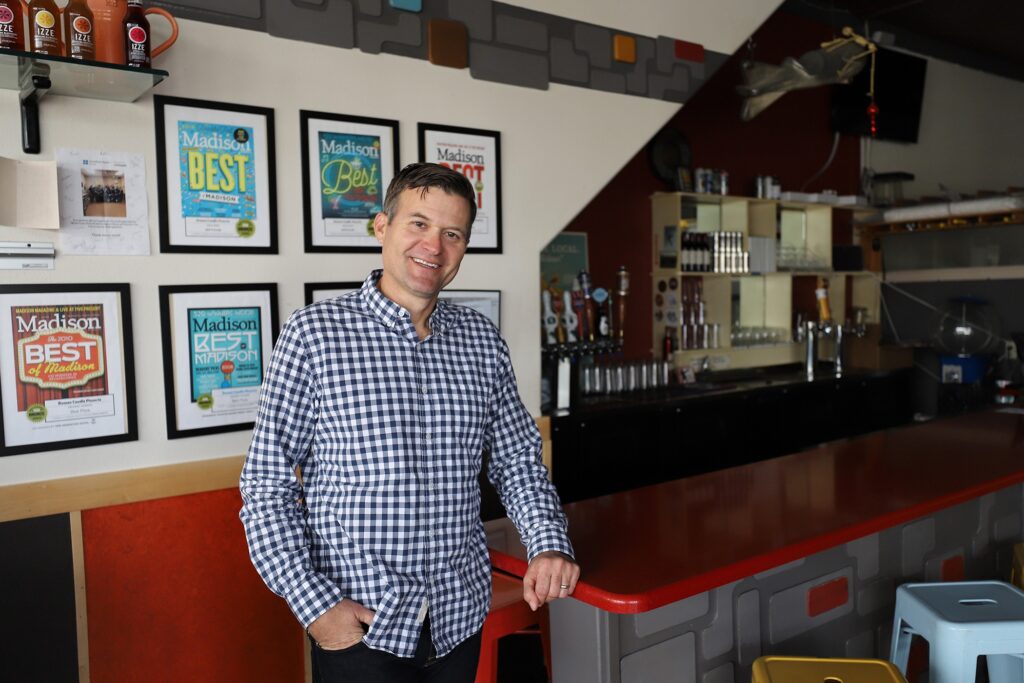 Brewer Stouffer, owner of Roman Candle Pizzeria, stands next to front counter; framed awards behind on wall