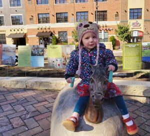 a little girl sitting on top of a horse statue