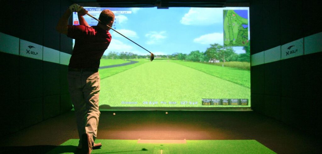 a man swinging a golf club in front of a large screen