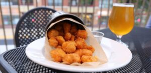 a white plate topped with tater tots next to a glass of beer