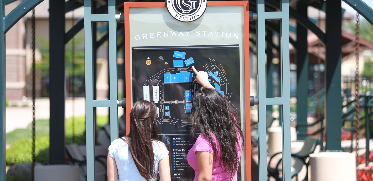 two girls standing in front of a greenway station sign
