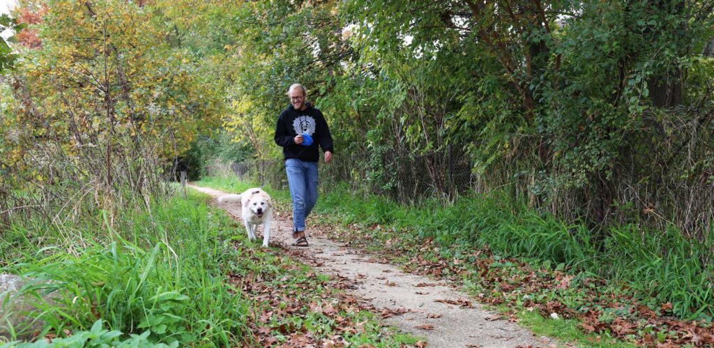 a woman walking her dog down a path in the woods