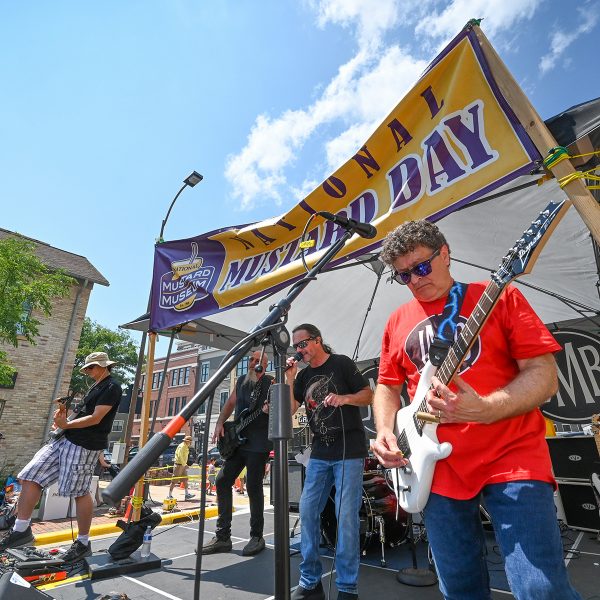 The National Mustard Day band performs on stage, three men with instruments.