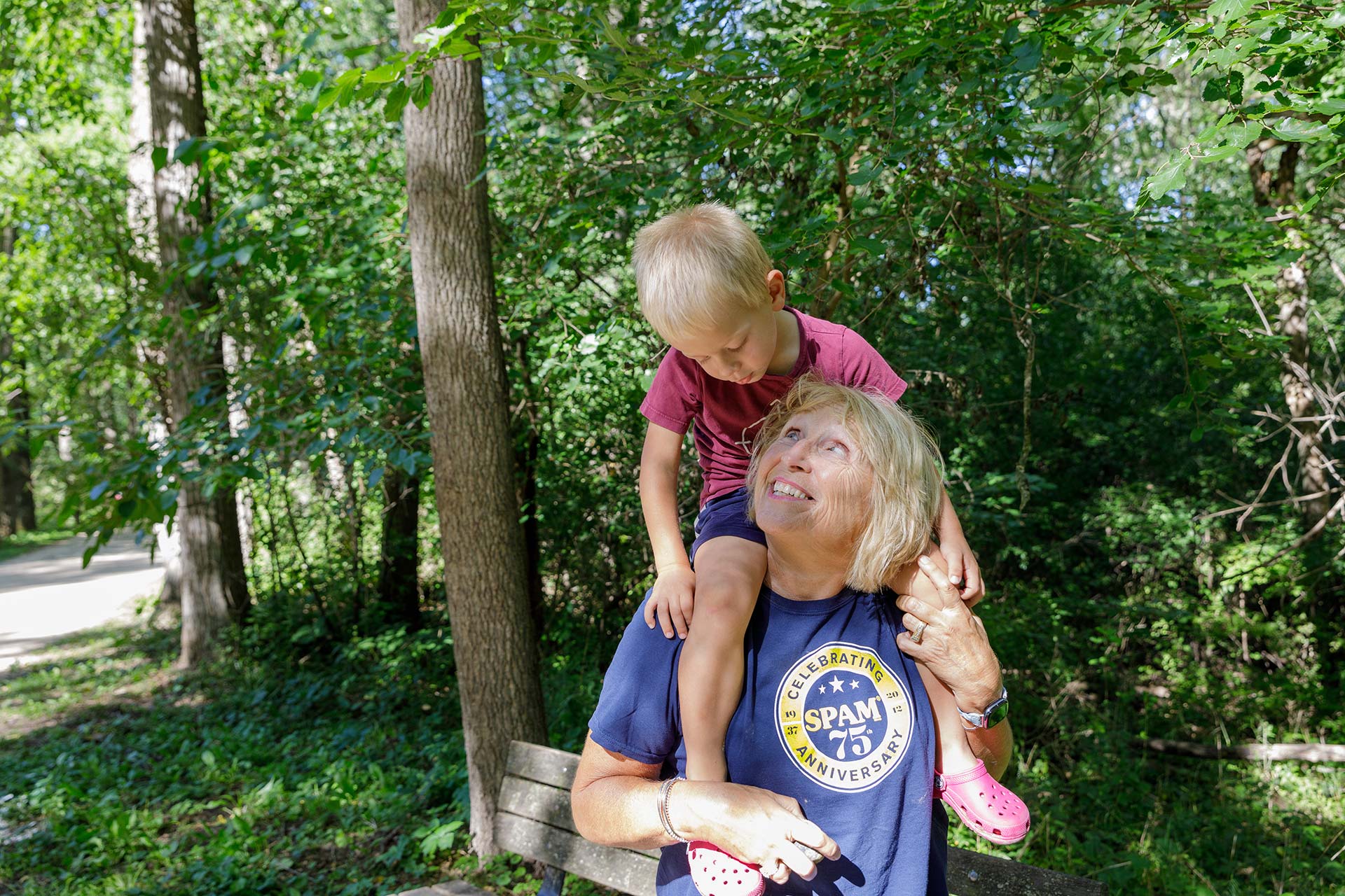 a woman sitting on a park bench with a child on her shoulders