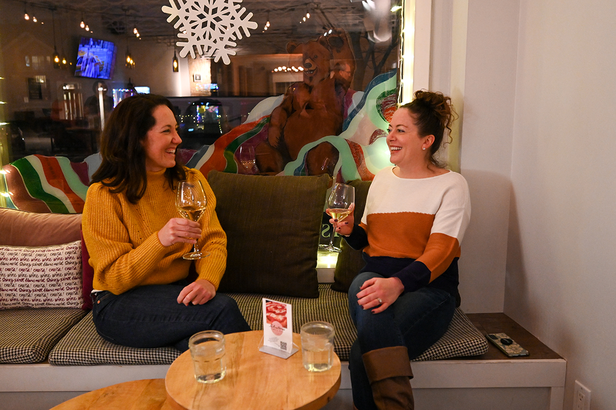 Two women sitting on a couch with wine glasses.