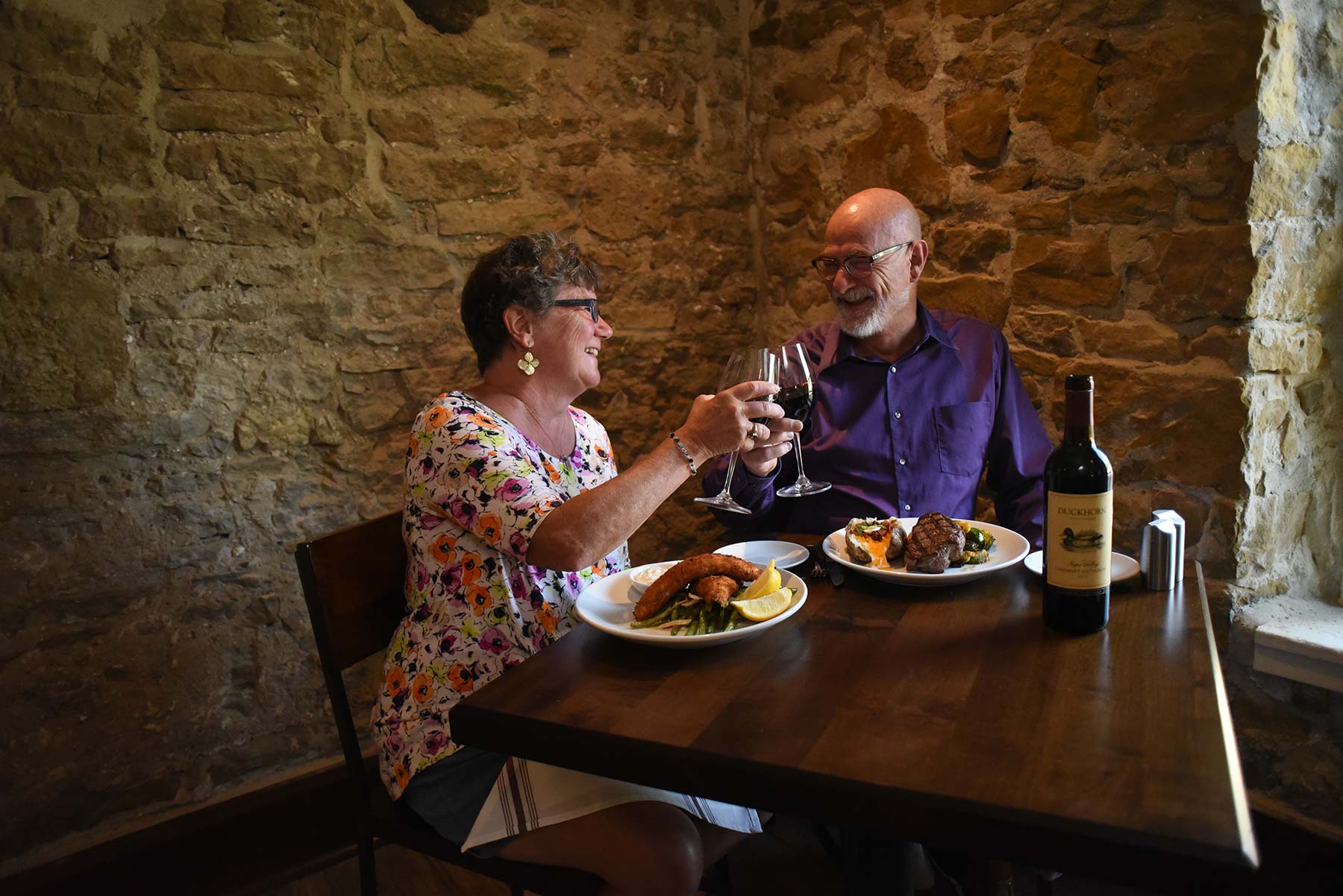 a man and woman sitting at a table drinking wine