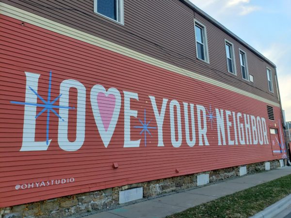 A large mural on the side of a building displays the words "LOVE YOUR NEIGHBOR" in white capital letters on a red background.