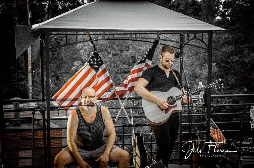 a man playing a guitar next to a man with an american flag on his head.
