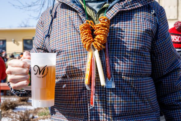 At Bockfest, a person wearing a pretzel necklace adorned with cheese sticks clutches a beer mug, celebrating the lively winter festival in true Middleton style.