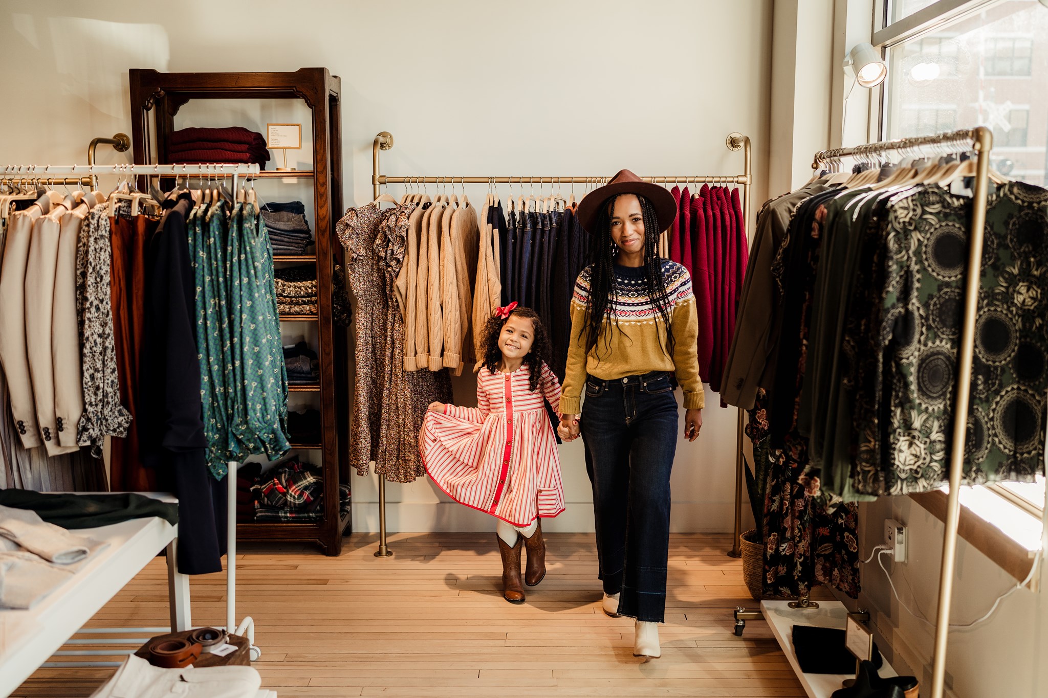a woman and a little girl standing in front of a rack of clothes.