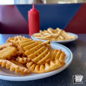 waffle fries are on a plate next to a bottle of ketchup.