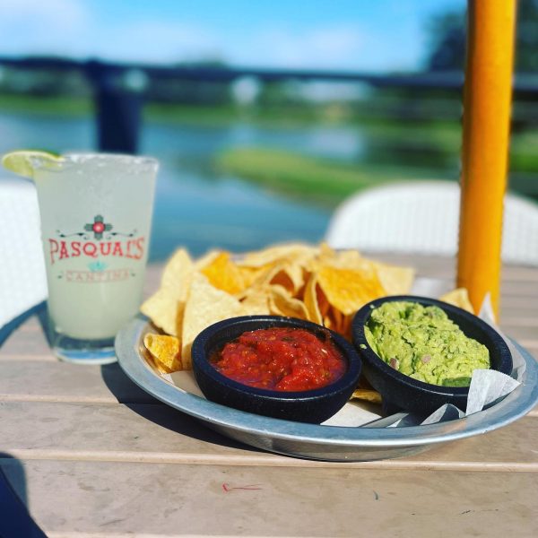 A plate of chips and guacamole on a table next to a drink.