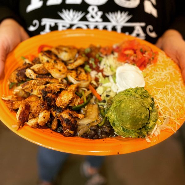A person holding up a plate of mexican food.