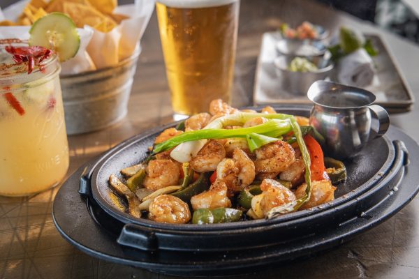 A plate with shrimp, peppers and chips on a table.