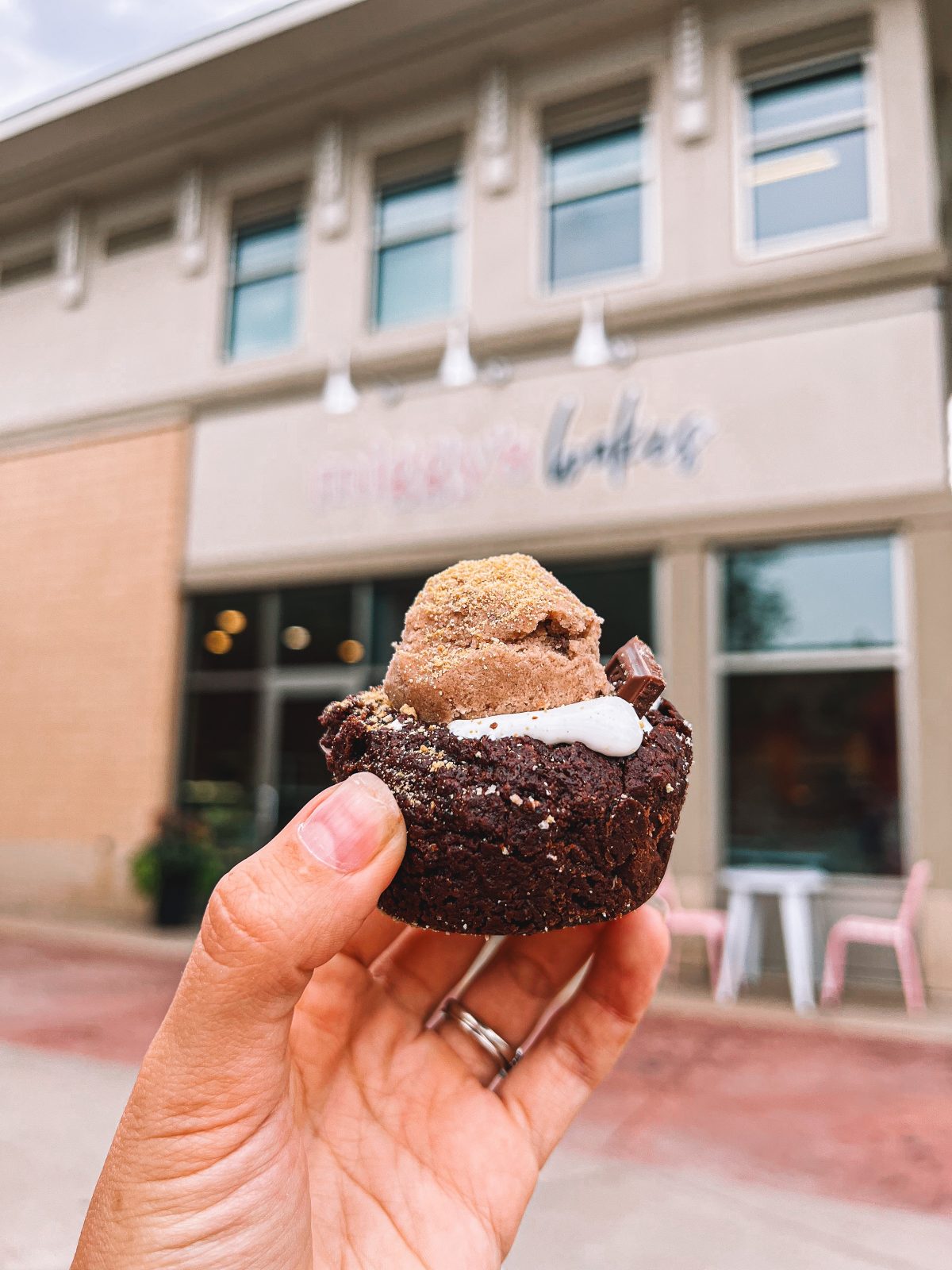 A person holding up a chocolate ice cream cupcake in front of a building.
