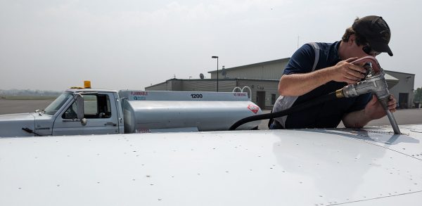 A man is filling a fuel tank on a plane.