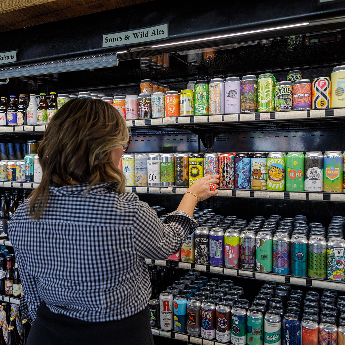 A woman choosing a beer from a shelf in a store.