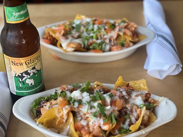 Two bowls of nachos next to a bottle of beer.
