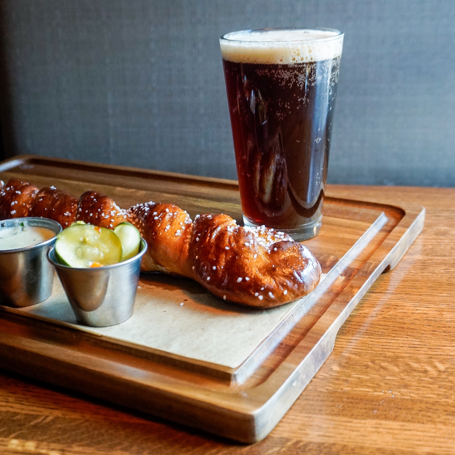 A pretzel and a glass of beer on a wooden tray.