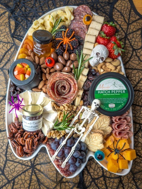 Halloween-themed charcuterie board with skeletons and local food on a ghost-shaped platter