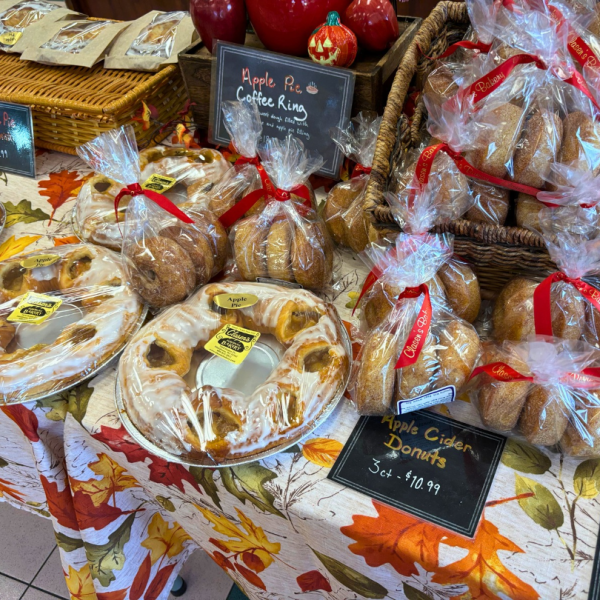 A display of glazed apple pie coffee rings and bags of apple cider donuts on a fall-themed tablecloth.