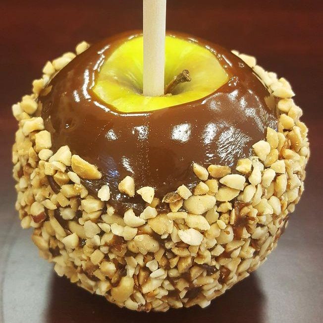 A chocolate covered apple with nuts on top.