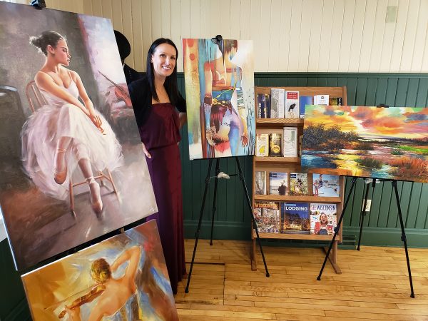 A woman standing next to several paintings on easels.