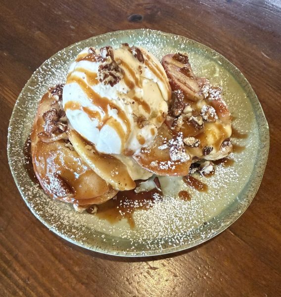 A scoop of ice cream on top of sliced apples, drizzled with caramel sauce and topped with pecans.