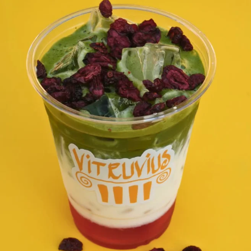 A layered iced matcha drink in a Vitruvius branded plastic cup topped with dried berries.