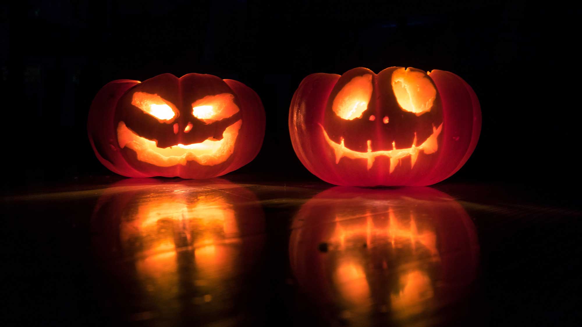 Two carved pumpkins are lit up in the dark.