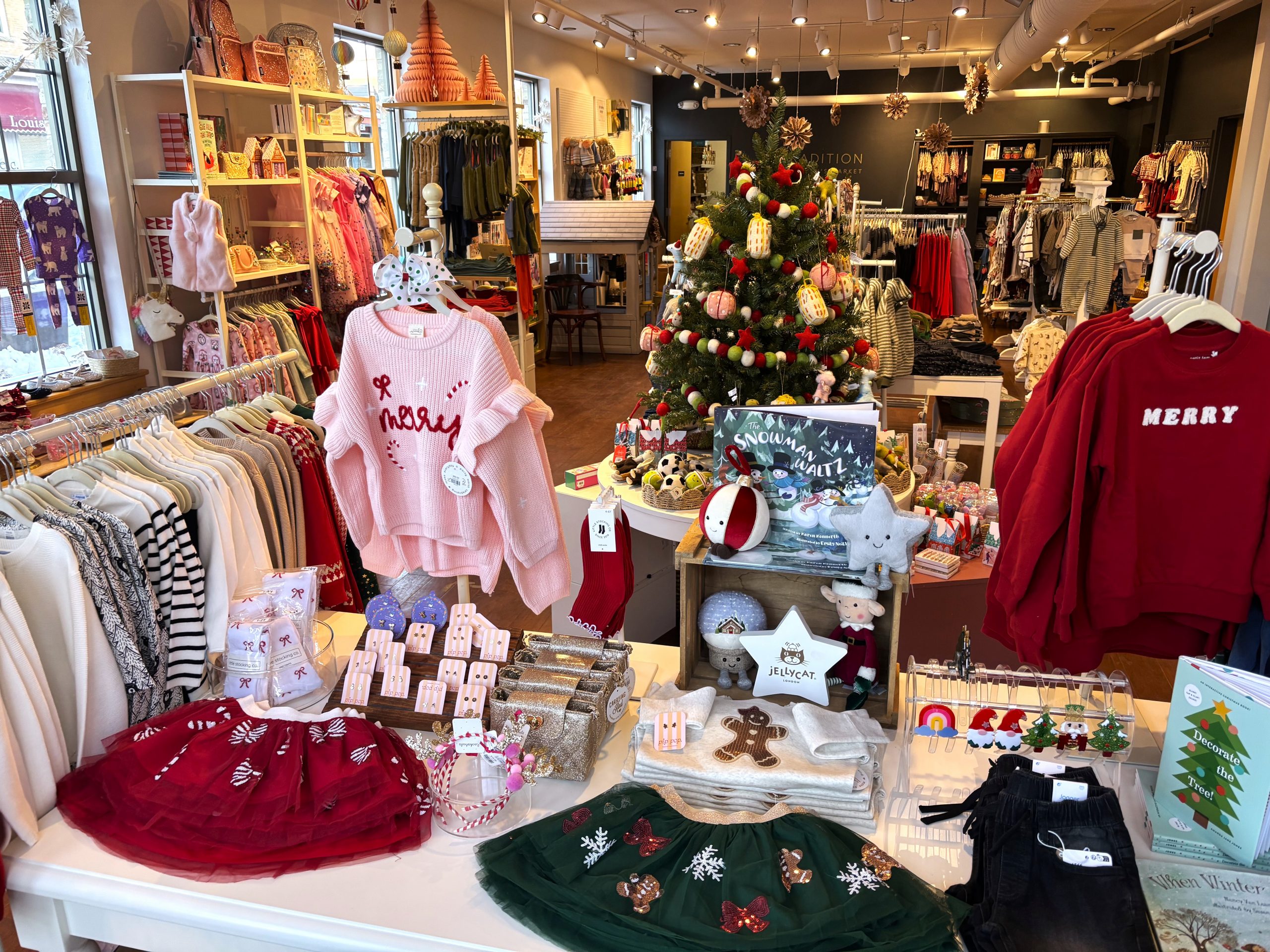 A children's clothing store displays festive holiday outfits and accessories, with a decorated Christmas tree and seasonal decor throughout the shop.