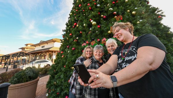 Three women are taking a picture in front of a christmas tree.