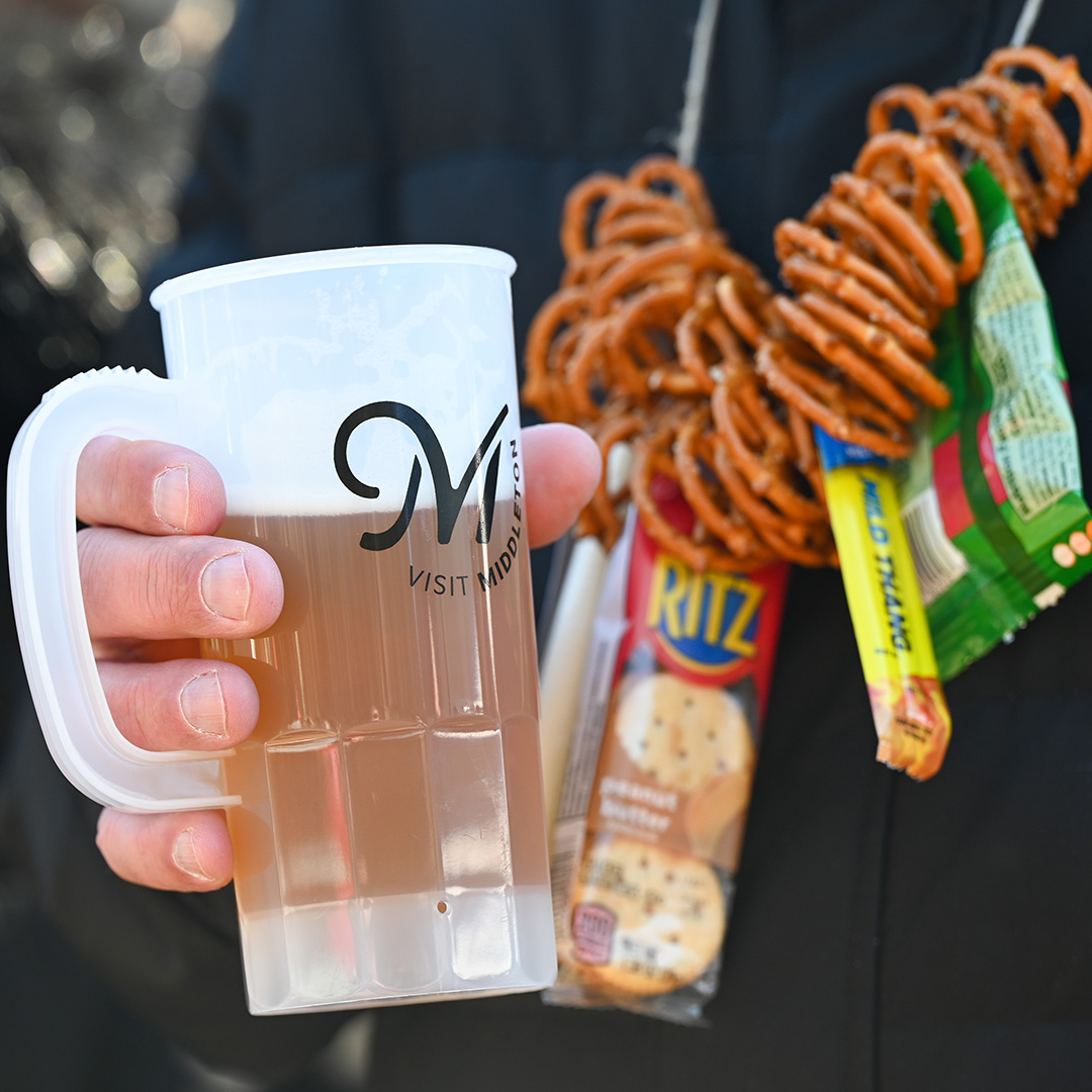 A person holding a cup of beer and pretzels.
