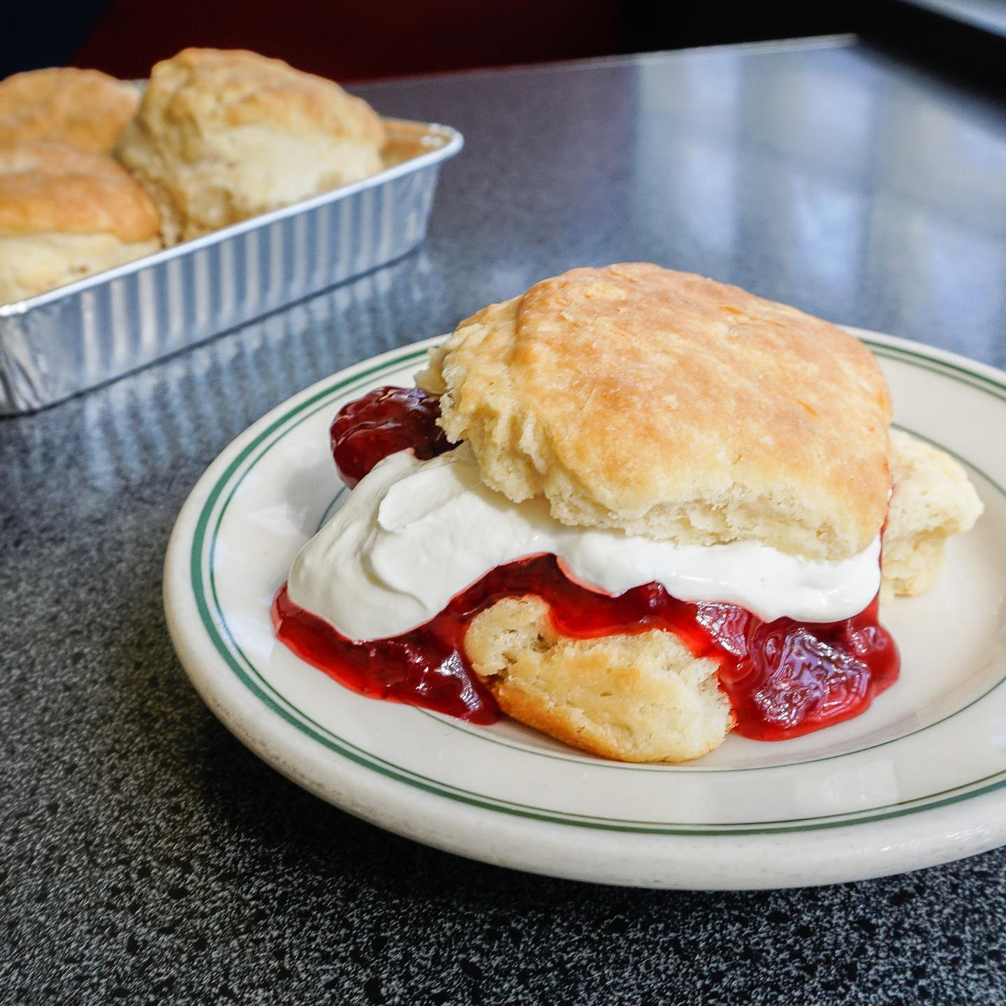 A plate of scones with whipped cream and strawberry jam.