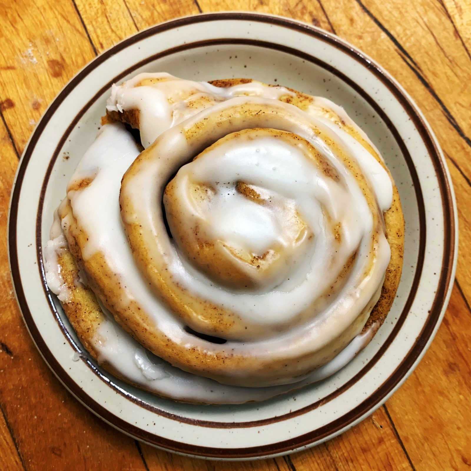 A cinnamon roll is sitting on a plate on a wooden table.